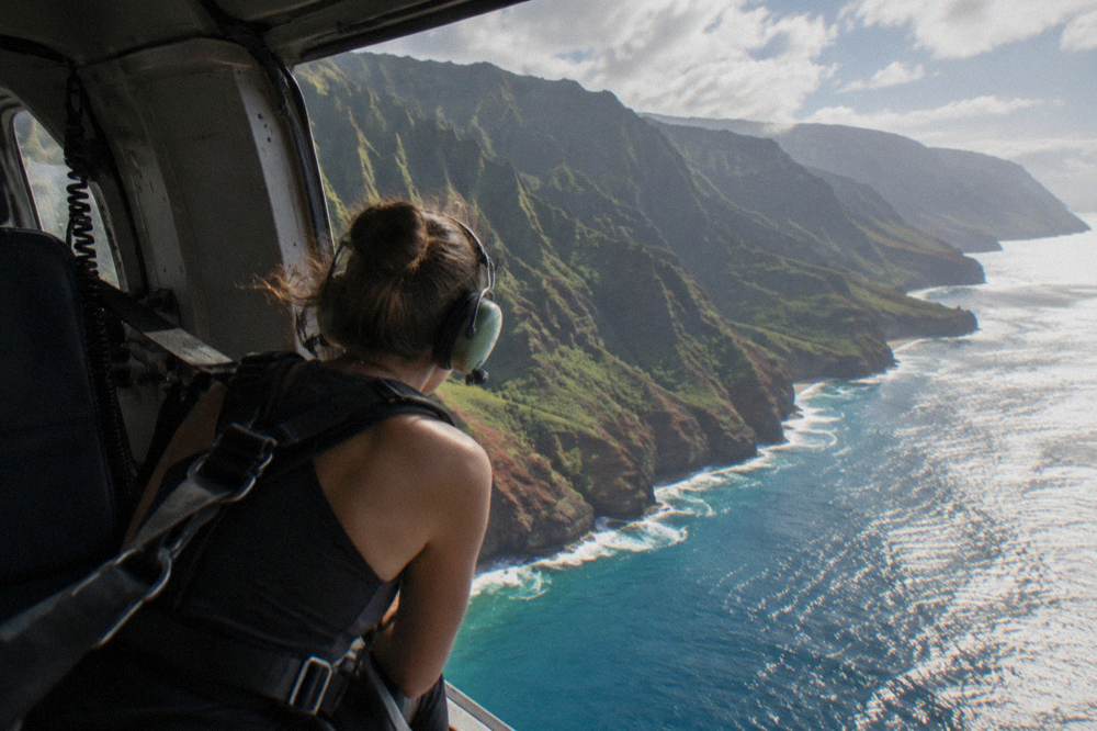 A doors-off helicopter in flight over the coast with passengers secured in harnesses