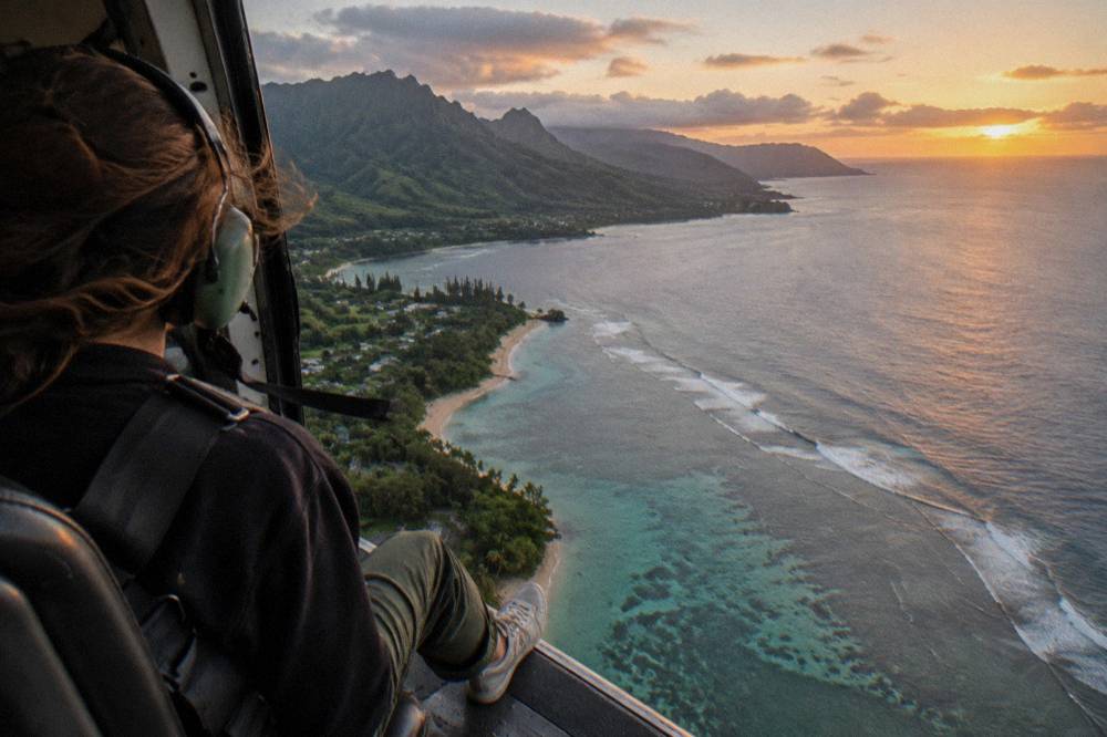 An open helicopter door with a passenger in a harness over the Kauai coast